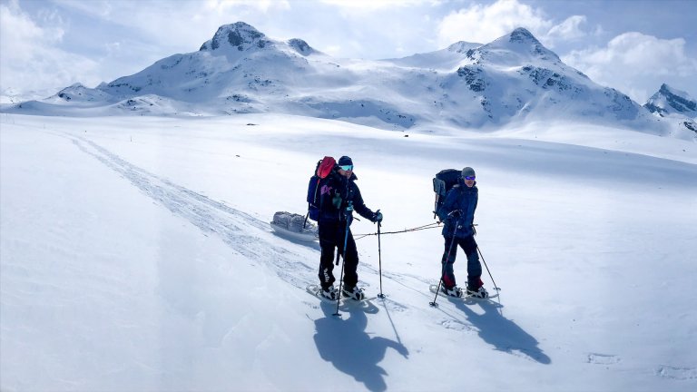 To menn i solskinn over snøkledde vidder med truger