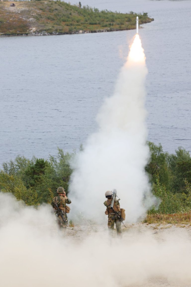 To soldater står på en topp over vannet, og et missil er nettopp skutt ut av et bærbart luftvernsystem på den ene soldatens skulder.