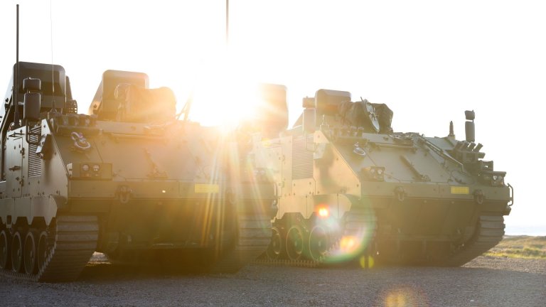 To grønne beltegående kjøretøy fotografert forfra med lav sol i bakgrunnen.